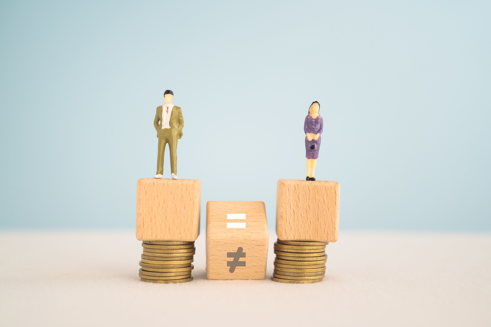 Gender pay equality concept. Man and woman icon  on wooden cube block and hand flipped unequal to equal sign with blurred stack of coins